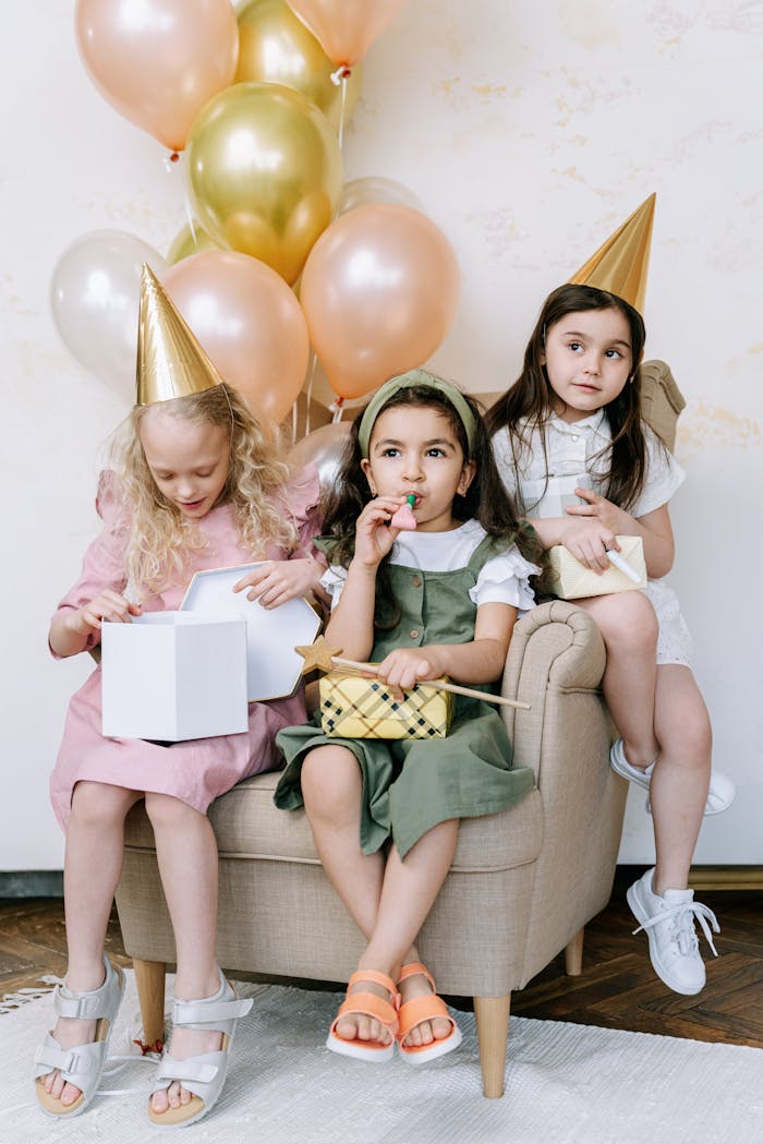 Three young girls enjoying a vibrant birthday party with balloons and gifts.